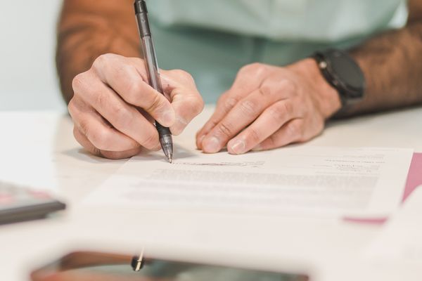 Gros plan sur un homme signant un document officiel avec un stylo à bille sur un bureau.