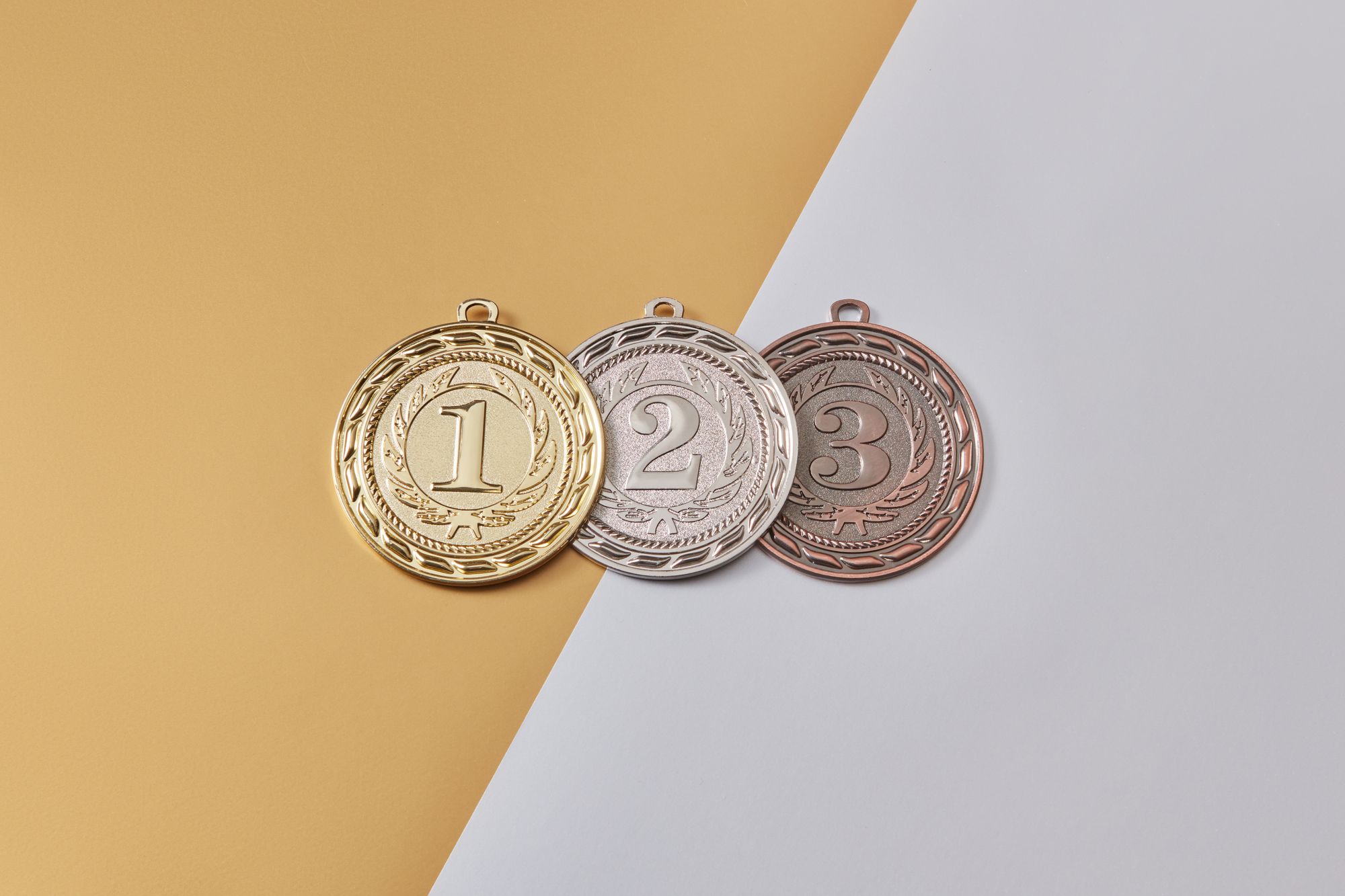 Médailles d'or, d'argent et de bronze disposées sur un fond moderne bicolore, symbolisant la réussite.