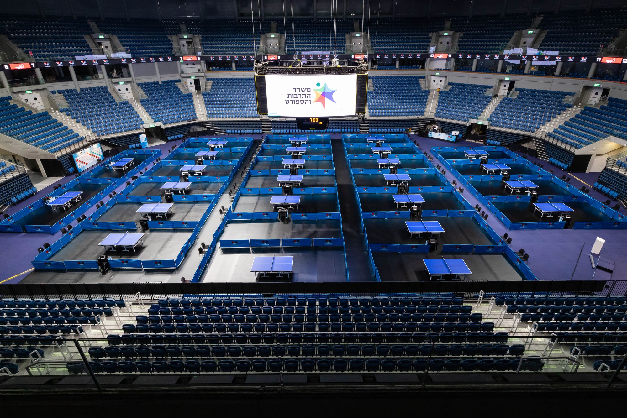 Vue aérienne d'une grande salle aménagée pour un tournoi de tennis de table avec de nombreuses tables.