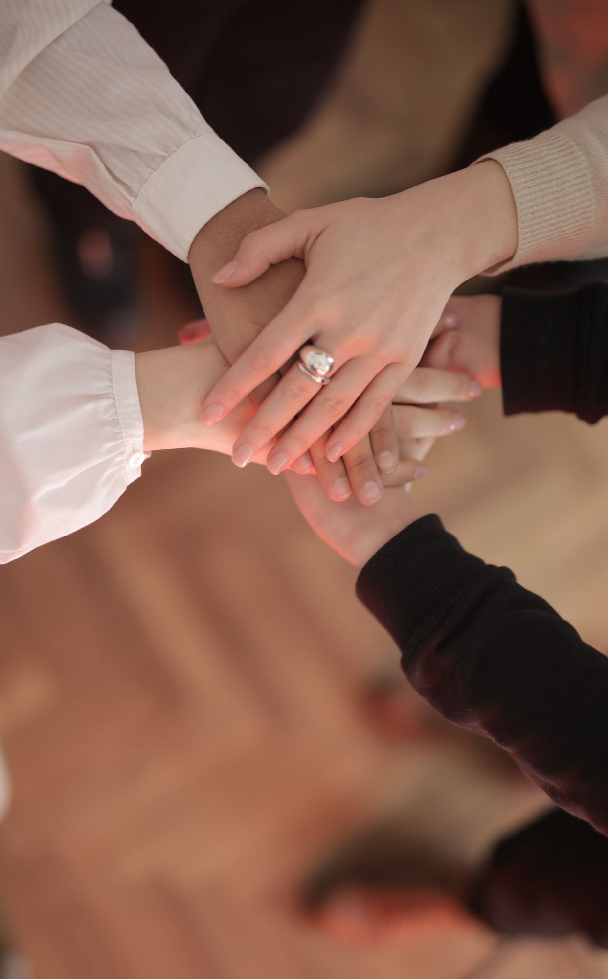 Vue de dessus d'amis sans visage, vêtus de tenues variées, empilant leurs mains alors qu'ils se tiennent debout sur un parquet en bois, à l'intérieur, par une journée ensoleillée.